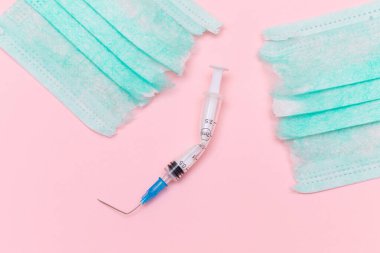 Aşı Karşıtı Hareket ve Maske Karşıtı Konsept - Kırık Tıbbi Şırınga ve Pembe Arkaplanda Yeşil Yırtık Tıbbi Maske. Salgın ve Kilitlenme Sonu - Üst Görünüm, Düz Yat