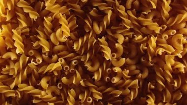 Pişmemiş Fusilli ve Chifferi Rigati Pasta Üst Manzara, Alçak Anahtar Işığı. Şişman ve Sağlıksız Yemek. Klasik Kuru Makarna, Yavaşça Dönen Arkaplan. Raw Different Macaroni Makarna Dokusunu Sola Döndür