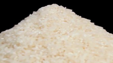 Beyaz Tabakta pişmemiş beyaz pirinç yığını Siyah Arkaplan 'a karşı dönüyor. Çiğ Uzun Taneli Pirinç Yığını. Asya mutfağı ve kültürü. Sağlıklı beslenme malzemeleri. Diyet Yemekler