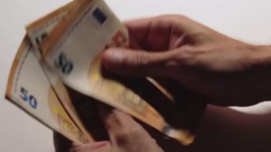 Elde Para Saymak. Avrupa Birliği Parası. Beyaz Adam Beyaz Masa 'da 50 Euro' luk banknot sayıyor. Turuncu Kağıt Nakit. Elde Elli Euro. Gelir, Tasarruf ve Harcama Konsepti