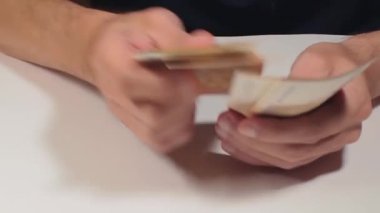 Elde Para Saymak. Avrupa Birliği Parası. Beyaz Adam Beyaz Masa 'da 50 Euro' luk banknotlar sayıyor. Turuncu Kağıt Nakit. Elde Elli Euro. Gelir, Tasarruf ve Harcama Konsepti