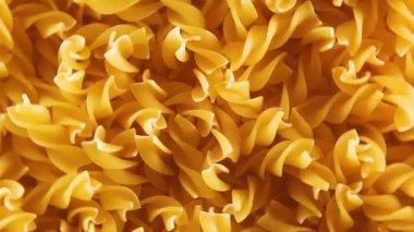 Pişmemiş Fusilli Makarna - Üst Görünüm, Yakın Çekim, Alçak Anahtar Işığı. Şişman ve Sağlıksız Yemek. Kuru Spiral makarna, döner arka plan. İtalyan Kültür ve Mutfağı. Çiğ Altın Makarna deseni. Sağ Çevirme