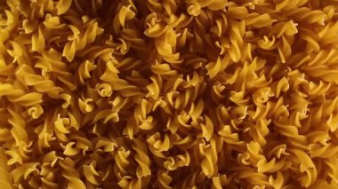 Uncooked Fusilli Pasta - Top View. Fat and Unhealthy Food. Dry Spiral Macaroni, Slowly Rotating Background. Italian Culture and Cuisine. Raw Golden Pasta Pattern. Left Rotation, Low Key Light