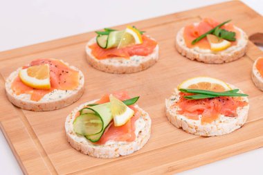 Taze somonlu pirinç keki sandviçler, salatalık, limon ve yeşillikler Bambu kesim tahtasında. Diyet yemek. Hızlı ve sağlıklı sandviçler. Taze dolgulu çıtır ekmek. Sağlıklı Beslenme Atıştırmaları