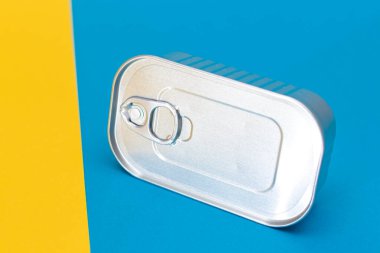 Bölünmüş mavi ve sarı arka plandaki teneke kutu. Konserve yiyecekler. Güvenli ve uzun vadeli yiyecek depolama için alüminyum kutu. Çelik Mühürlü Yiyecek Depolama Kutusu