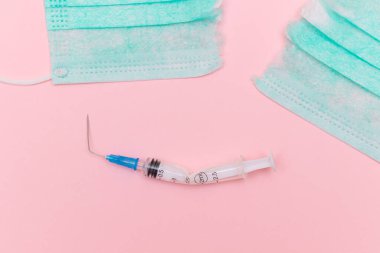 Aşı Karşıtı Hareket ve Maske Karşıtı Konsept - Kırık Tıbbi Şırınga ve Pembe Arkaplanda Yeşil Yırtık Tıbbi Maske. Salgın ve Kilitlenme Sonu - Üst Görünüm, Düz Yat