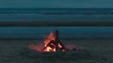 Dalgalı Deniz 'e karşı sahilde şenlik ateşi ya da Bulutlu Bir Zamanda Akşam' da Okyanus. Kum tepesinde yanan kamp ateşi. Ateşe odun. Şenlik Ateşi için yer. Deniz kenarındaki ateş çukuru. Sinyal Ateşi - Sabit Çekim, Yavaş Hareket