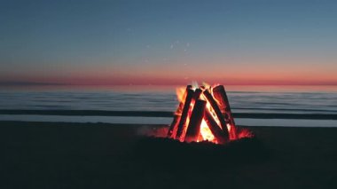 Sahil kıyısındaki renkli şenlik ateşi ya da Dark Romantic Evening 'de okyanusa karşı - Ağır çekim. Kamp ateşi Kum üzerinde yanıyor. Ateşe odun. Şenlik Ateşi için yer. Deniz kenarındaki ateş çukuru. İşaret için Ateş