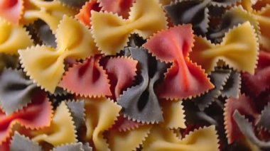 Pişmemiş Renkli Farfalle Makarnası: Çok Renkli Papyonlu Makarna Mutfak Tuvali, Dokulu Arka plan - Üst Görünüm, Açısal Dönme. Renkli Kuru Makarnaya Dönüş. Çiğ makarna - Döndürme