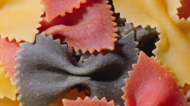 Pişmemiş Renkli Farfalle Makarnası: Çok Renkli Papyonlu Makarna Mutfak Tuvali, Dokulu Arka plan - Üst Görünüm, Açısal Dönme. Renkli Kuru Makarnaya Dönüş. Çiğ makarna - Döndürme
