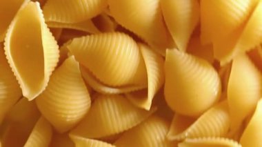 Pişmemiş Conchiglie Pasta: Konchiglie Macaroni 'nin Mutfak Tuvali, Gurme Yemekleri İçin Canlı ve Dokulu Bir Arkaplan Oluşturma - Döndürme. Kuru makarnaya dönüşüyor. Çiğ makarna - Yan Döndürme