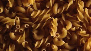 Pişmemiş Fusilli ve Chifferi Rigati Pasta Üst Manzara, Alçak Anahtar Işığı. Şişman ve Sağlıksız Yemek. Klasik Kuru Makarna, Yavaşça Dönen Arkaplan. Raw Different Macaroni Makarna Dokusunu Sola Döndür