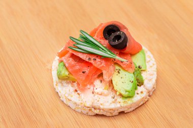 Taze somonlu Rice Cake Sandviçi, Bambu Kesme Kurulunda Avokado ve Zeytinler. Kolay Kahvaltı 'da. Diyet yemek. Hızlı ve sağlıklı sandviçler. Lezzetli dolgulu kızarmış ekmek. Sağlıklı Beslenme Atıştırması