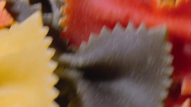 Pişmemiş Renkli Farfalle Makarnası: Çok Renkli Papyonlu Makarna Mutfak Tuvali, Dokulu Arka plan - Üst Görünüm, Açısal Dönme. Renkli Kuru Makarnaya Dönüş. Çiğ makarna - Döndürme