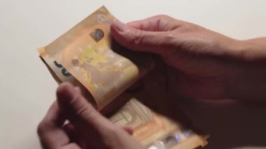 Elde Para Saymak. Avrupa Birliği Parası. Beyaz Kadın Beyaz Masa 'da 50 Euro' luk banknotlar sayıyor. Turuncu Kağıt Nakit. Elde Elli Euro. Gelir, Tasarruf ve Harcama Konsepti