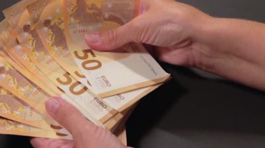 Elde Para Saymak. Avrupa Birliği Parası. Siyah Masa 'ya 50 Euro' luk banknotlar sayan Beyaz Kadın - Yakın plan. Turuncu Kağıt Nakit. Elde Elli Euro. Gelir, Tasarruf ve Harcama Konsepti