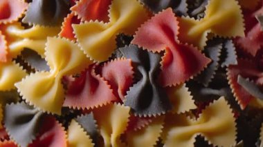 Pişmemiş Renkli Farfalle Makarnası: Çok Renkli Papyonlu Makarna Mutfak Tuvali, Dokulu Arka plan - Üst Görünüm, Açısal Dönme. Renkli Kuru Makarnaya Dönüş. Çiğ makarna - Döndürme