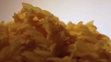 Uncooked Fusilli Pasta Heap Rotating against White Background. Fat and Unhealthy Food. Dry Spiral Macaroni. Italian Culture and Cuisine. Raw Golden Pasta