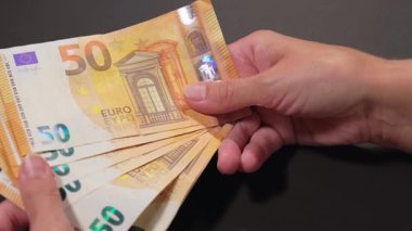Elde Para Saymak. Avrupa Birliği Parası. Siyah Masa 'ya 50 Euro' luk banknotlar sayan Beyaz Kadın - Yakın plan. Turuncu Kağıt Nakit. Elde Elli Euro. Gelir, Tasarruf ve Harcama Konsepti