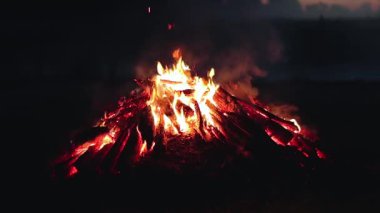 Big Campfire is Burning Down in Early Morning or Evening against the Blue Sky. Wood on Fire. Flying Sparks. Travel and Tourism Concept. Remains of a Giant Bonfire at Summer - Static Shot, Slow Motion