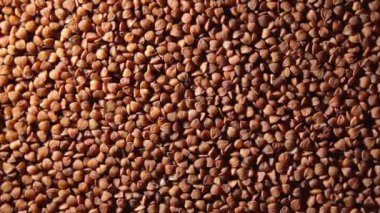Kuru pişmemiş kahverengi karabuğday Groats, Yavaşça Dönen Arkaplan Üst Görünüm, Alçak Anahtar Işığı. Çiğ Büyük Karabuğday Taneleri. Rus, Ukrayna ve Beyaz Rusya Kültürü. Sağa Döndür