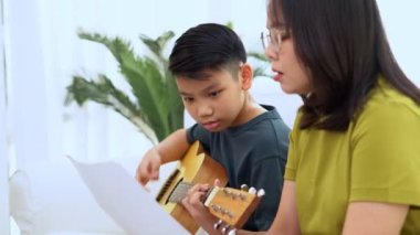 Asyalı anne, oğlu ve gitar çalan Asyalı çocuğu kucaklıyor ve annesi kanepede sarılıyor ve takdir edilip cesaretlendirildiğini hissediyor. Mutlu bir aile kavramı, öğrenme ve eğlenceli yaşam tarzı, aile bağlarını sevme