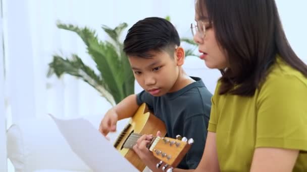 アジアの母親は息子を包含し アジアの少年はギターを演奏し 母親はソファに抱擁し 感謝し 奨励しています 幸せな家族 楽しいライフスタイル 家族の絆の概念 — ストック動画