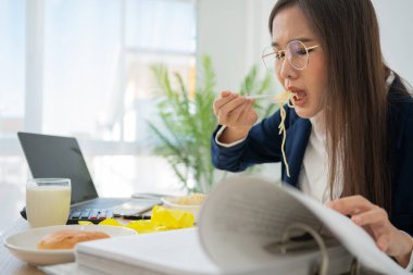 Busy and tired businesswoman eating spaghetti for lunch at the Desk office and working to deliver financial statements to a boss. Overworked and unhealthy for ready meals, burnout concept.