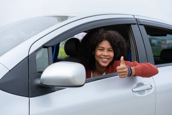 若い女性の半分のアジアの半分アフリカは 新しい現代の車の中に親指を表示します パスドライバー免許試験後の若い女性の興奮最初の道路の旅 新しい車を手に入れた後は気分がいい — ストック写真