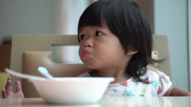 Mutfaktaki masada kahvaltı yapmak için kaşıkla mısır gevreği toplayan mutlu bir Asyalı çocuk. Kavramsal Kahvaltı çocuk ve çocuğun sağlıklı büyümesi için önemli bir yemektir..