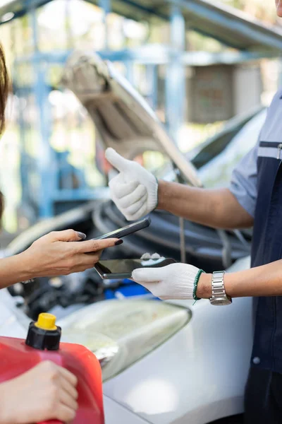 Asian women get contact numbers from auto mechanics after fixing the car engine problem and QR code scan to pay for gas after running out of fuel on the road. Car repair and maintenance concept.