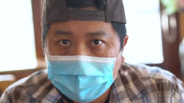 Medikal maskeli orta yaşlı bir adamın yakın plan portresi. Kameraya, Coronavirus COVID-19 'a ve hava kirliliği koruma konseptine bakıyor..