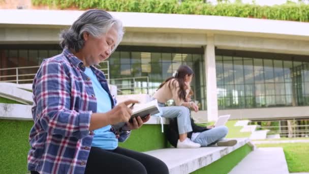 上完大学后 成熟的成年学生坐在大学楼前面看书 成人教育学习快乐的亚洲老年人退休活动 — 图库视频影像