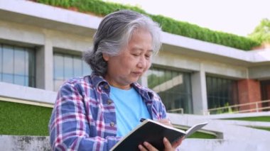Yetişkin bir öğrenci üniversite binasının önünde oturuyor ve bir üniversite dersine katıldıktan sonra okul kitapları okuyor, Yetişkin Eğitimi Öğreniyor Mutlu Asyalı Yaşlılar aktivitelerini inceliyor.