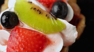 Waffle üzerindeki tatlı meyve ve krema, dönen çilek, kivi, yaban mersinli ve bademli waffle 'ların yakın görüntüsü.