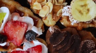 Waffle üzerindeki tatlı meyve ve krema, dönen çilek, kivi, yaban mersinli ve bademli waffle 'ların yakın görüntüsü.