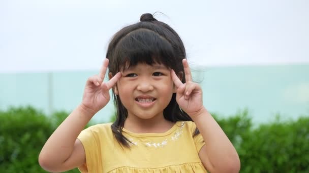 ポートレート面白い小さなアジアの女の子の大きな笑顔の子供は カメラを見て彼女の頬を指して 子供時代の証言の概念を楽しんで 肯定的な子供 4K映像 スローモーション肖像 — ストック動画