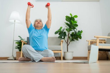Asian senior woman lifting dumbbell for exercise and workout at home. Active mature woman doing stretching exercise in living room. Exercise Active and healthy for older, elder, and senior concept.