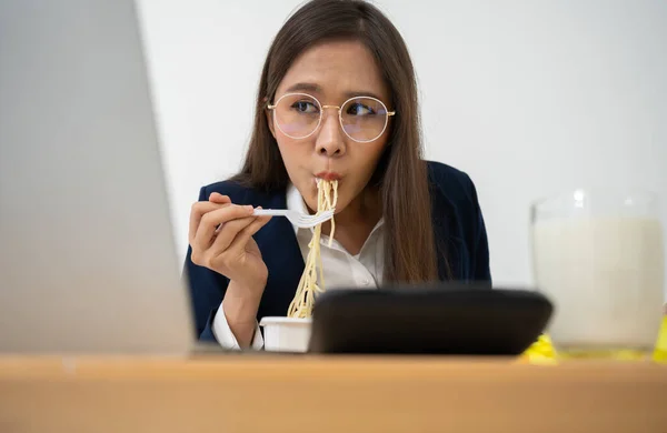 Busy and tired businesswoman eating spaghetti for lunch at the Desk office and working to deliver financial statements to a boss. Overworked and unhealthy for ready meals, burnout concept.