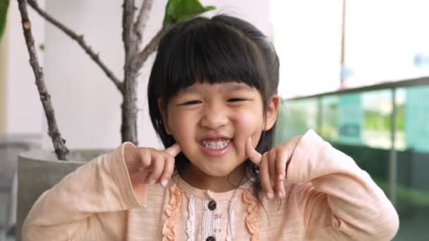 Портрет Смешная Маленькая Азиатская Девочка Большой Улыбающийся Ребенок Смотрящий Камеру — стоковое видео