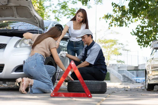 Expertise mechanic man  in uniform using force trying to unscrew the wheel bolts nuts and help a woman for changing car wheel on the highway, car service, repair, maintenance concept.