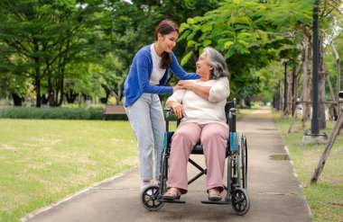 Tekerlekli sandalyedeki hastayla ilgilenen Asyalı dikkatli bir bakıcı ya da hemşire. Bakıcının, birikimin ve sağlık sigortasının özenle mutlu emeklilik kavramı. Mutlu bir aile.