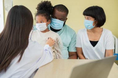 Asyalı kadın pediyatrist doktor muayene için stetoskop tutuyor küçük bir kız hasta ve çocuğun kalp ciğerleri, iyi aile doktoru çocuğu evde ziyaret ediyor, sağlık ve çocukluk konsepti için ilaç alıyor..