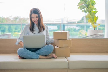 Mutlu Asyalı genç girişimci ev bilgisayarındaki bir dizüstü bilgisayardan siparişleri kontrol ettikten sonra satış başarısı için gülümseyin, İnternet ve e-ticaret ticaret sektörü kavramı