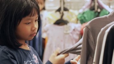Sevimli küçük kız alışveriş merkezindeki çocuk moda mağazasında bir sürü kıyafet arasından yeni bir elbise seçiyor. Satış, hediyeler, Noel, tatil güzelliği ve moda kavramı.