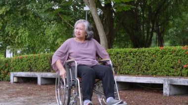 Happy alone Asian senior women sitting in wheelchair and pushing wheelchairs to move forward in the park, Concept of happy retirement with care from a caregiver and Savings and senior health insurance