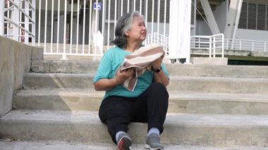 Mutlu ve gülümseyen yaşlı Asyalı kadın spor yaptıktan sonra merdivenlerde oturuyor, sabahları koşuyor, sağlıklı olmak için dışarıda kıdemli egzersizler yapıyor. Sağlıklı yaşam için sağlık ve aktif yaşam biçimi kavramı