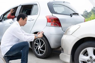 Asian men driver check for damage after a car accident before taking pictures and sending insurance. Online car accident insurance claim after submitting photos and evidence to an insurance company.