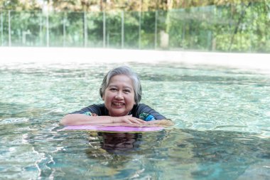 Young trainer helping senior woman in aqua aerobics and working out in the pool. old woman and mature man doing aqua aerobics exercise in swimming pool, Elderly sports, and active lifestyle concept.