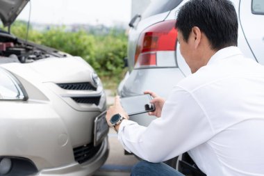 Asian men driver check for damage after a car accident before taking pictures and sending insurance. Online car accident insurance claim after submitting photos and evidence to an insurance company.